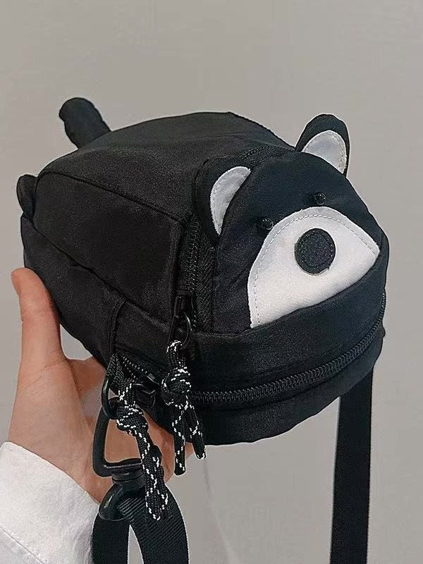 Black raccoon crossbody phone bag held in hand, face and ears on the lid