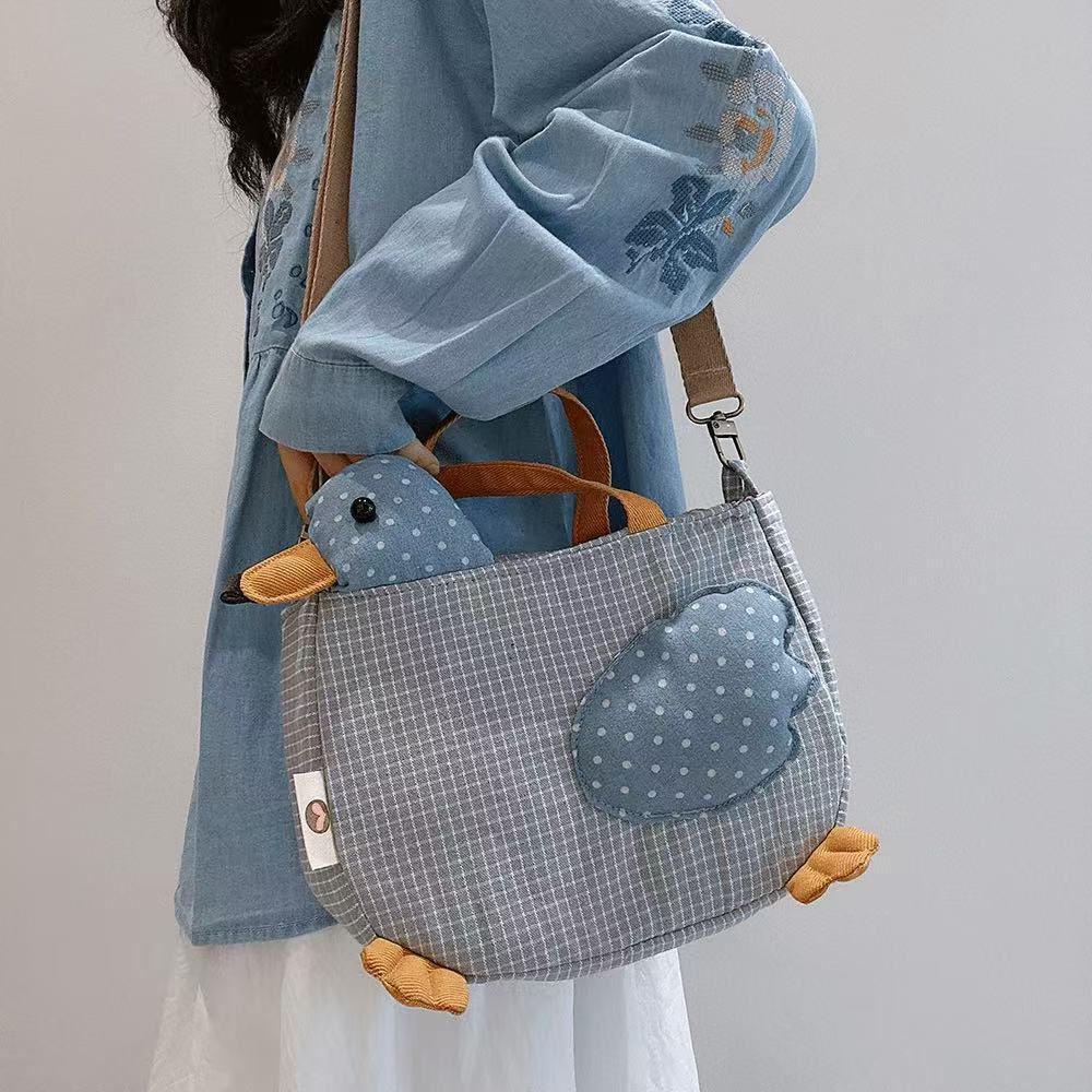 Blue check duck tote bag with stuffed polka-dot head worn on the shoulder