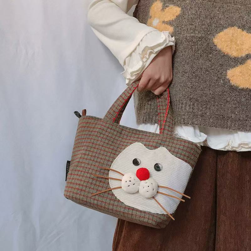 Plaid cat tote handbag with red pom-pom nose, held by the handles
