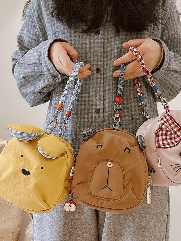 Yellow bunny, brown bear and pink cat mini crossbody bags held by their braided handles