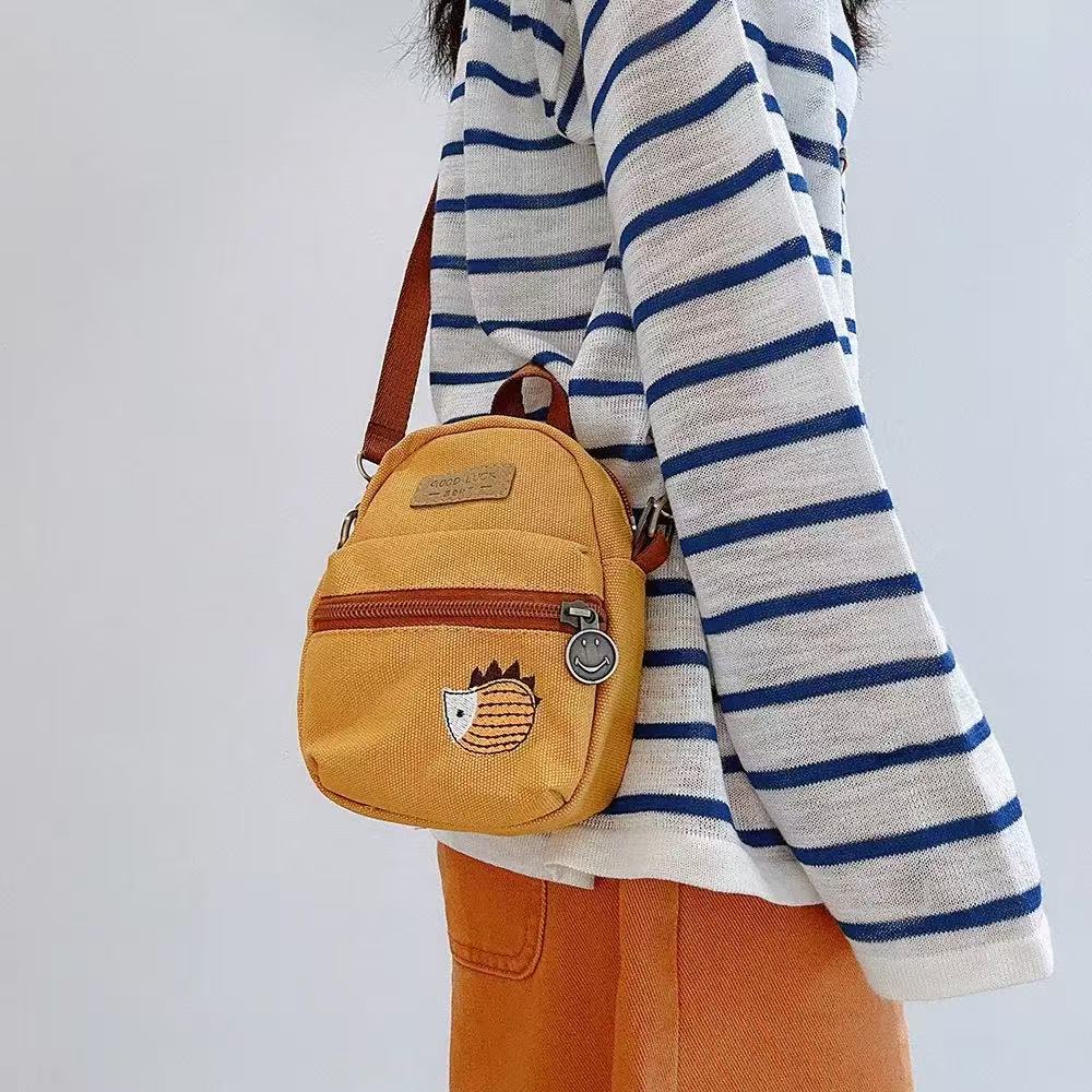 Mustard yellow canvas hedgehog phone bag worn crossbody with a striped top
