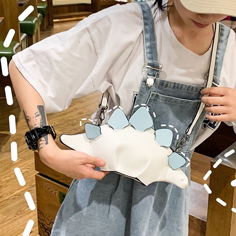 White stegosaurus bag worn crossbody over denim overalls