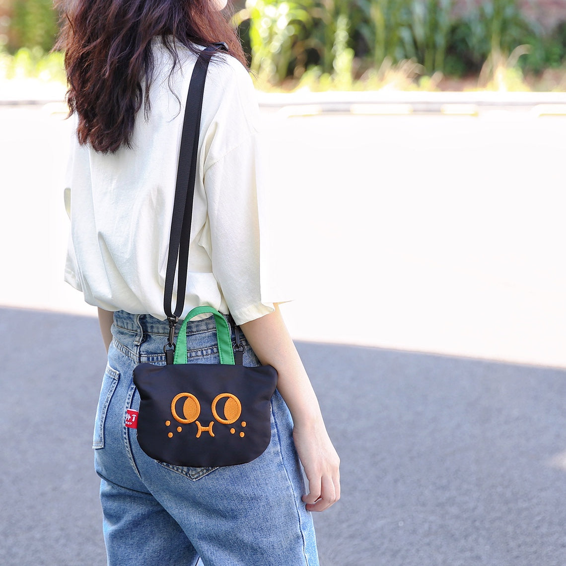 Black cat phone bag worn crossbody with jeans, seen from behind