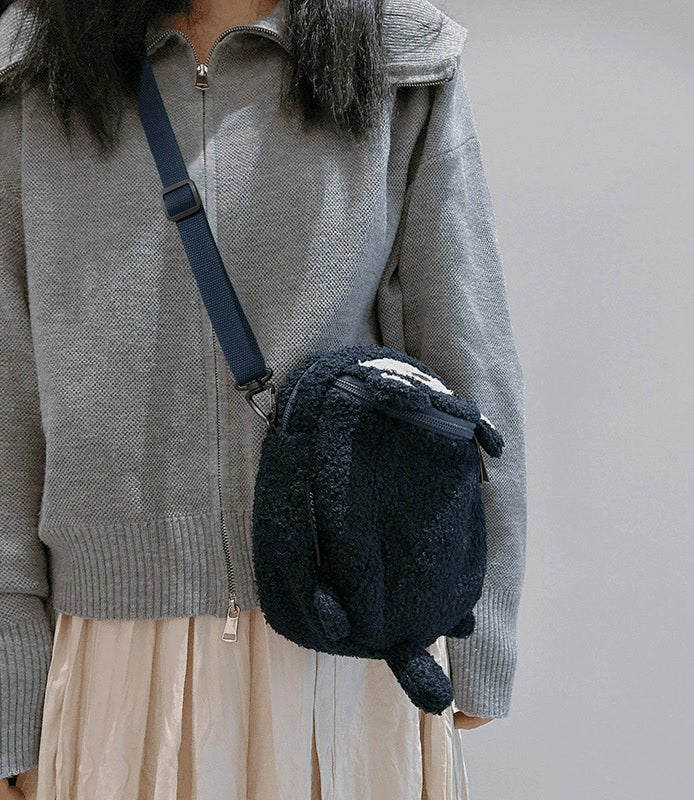Navy teddy fleece raccoon bag worn crossbody over a grey jacket