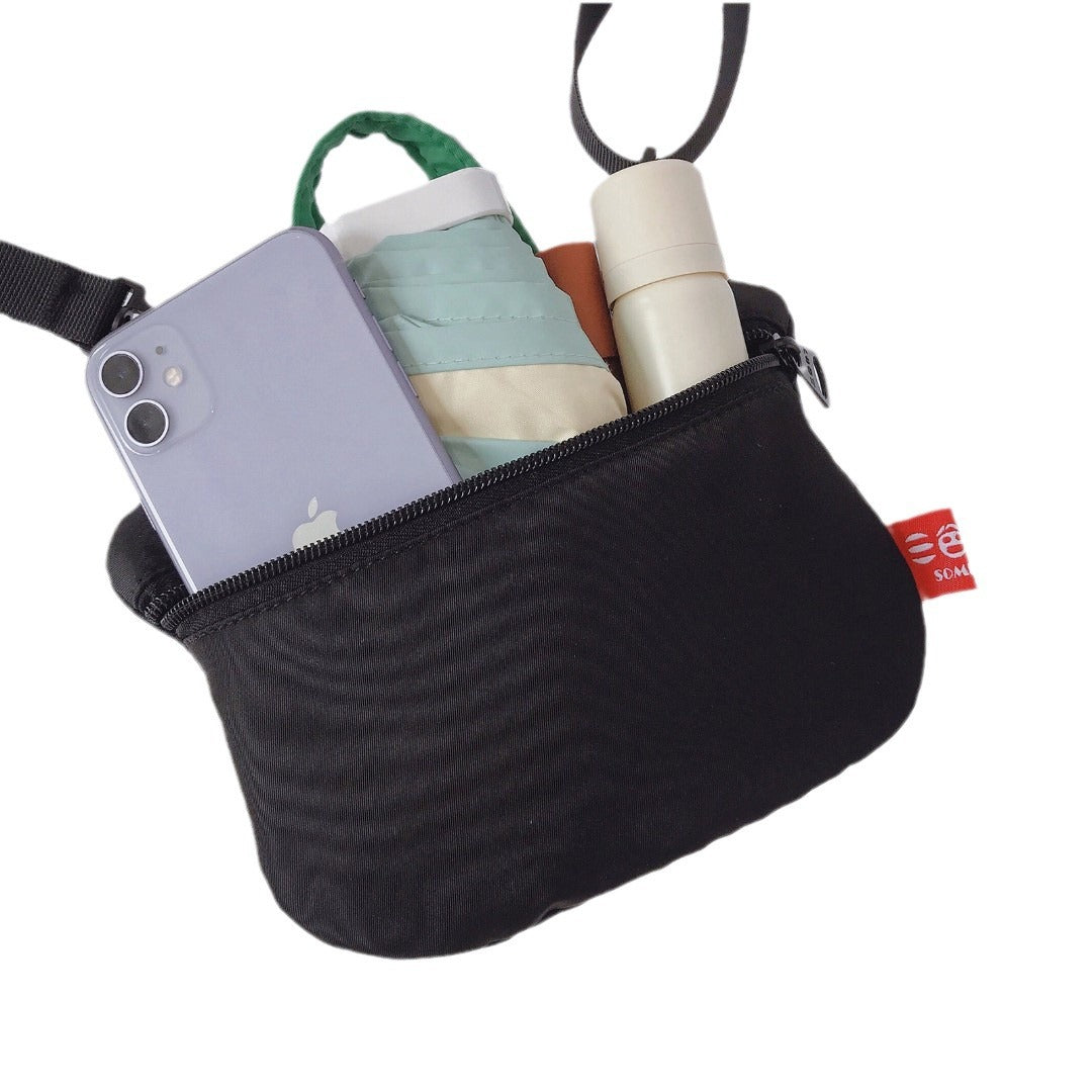 Back of the bag unzipped with a phone, folding umbrella and small bottle inside