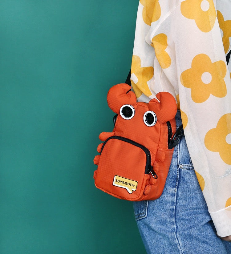 Orange crab bag at the hip against a teal wall